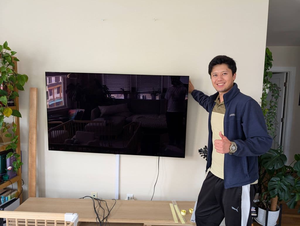 A wall mounted TV in a bright apartment living room with plants either side